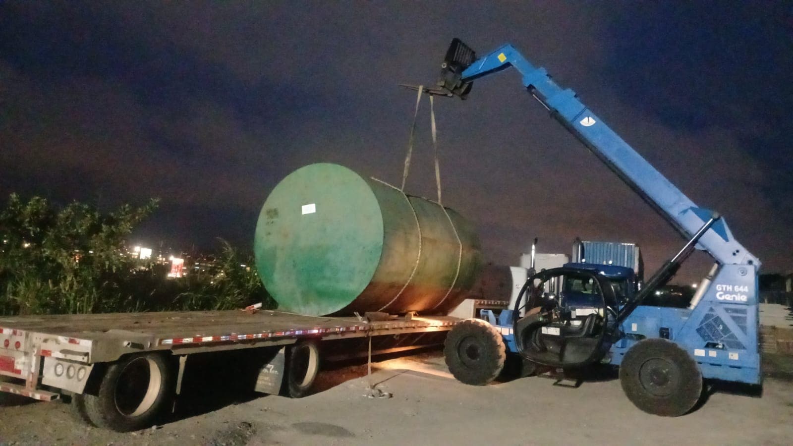 Telehandler subiendo un tanque verde a una plataforma, de noche