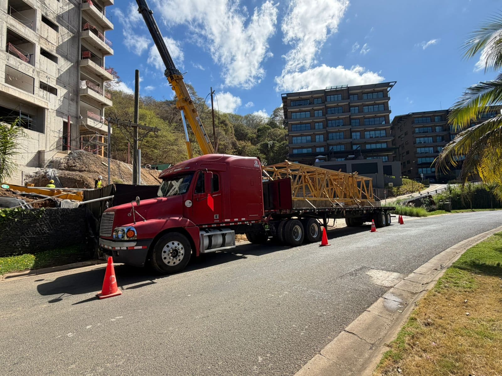 Cabezal rojo con secciones de grúa torre en la plataforma, junto a un edificio en construcción