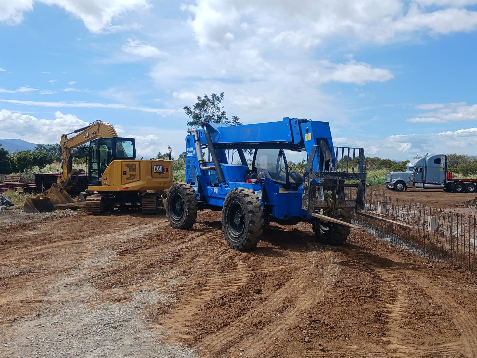 Telehandler Genie y excavadora CAT en un lote, con un cabezal al fondo